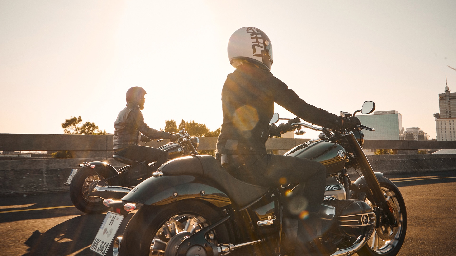 We see two motorcyclists in the sunshine.